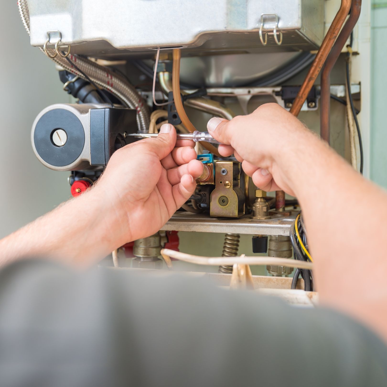 Hands adjusting boiler components with tools inside an open appliance, showing wiring and pipes.