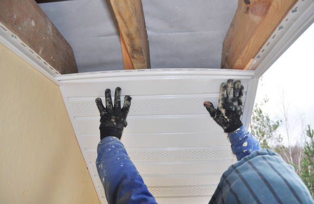 Black gloved hands of roof replacement contractor installing white fascia on roof with wooden beams.