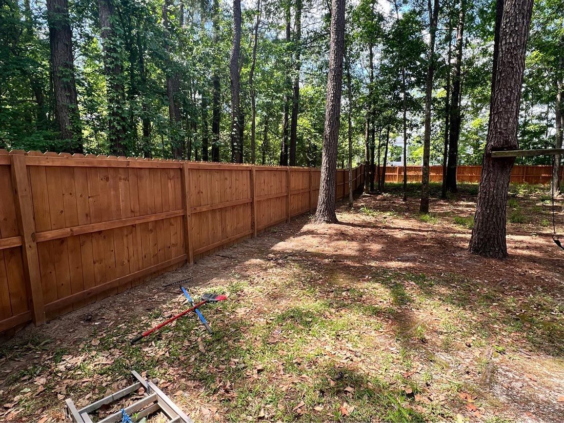 A wooden fence is surrounded by trees in a backyard.