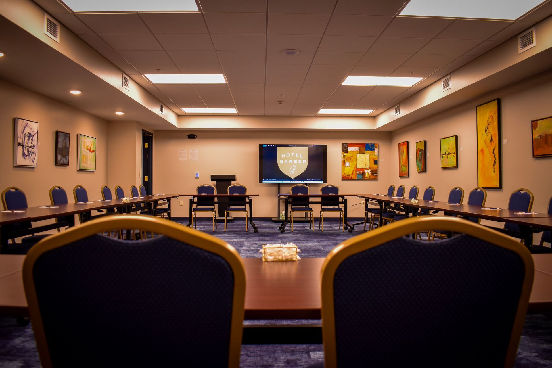 Conference room with dark blue chairs, U-shaped tables, and artwork on the walls.