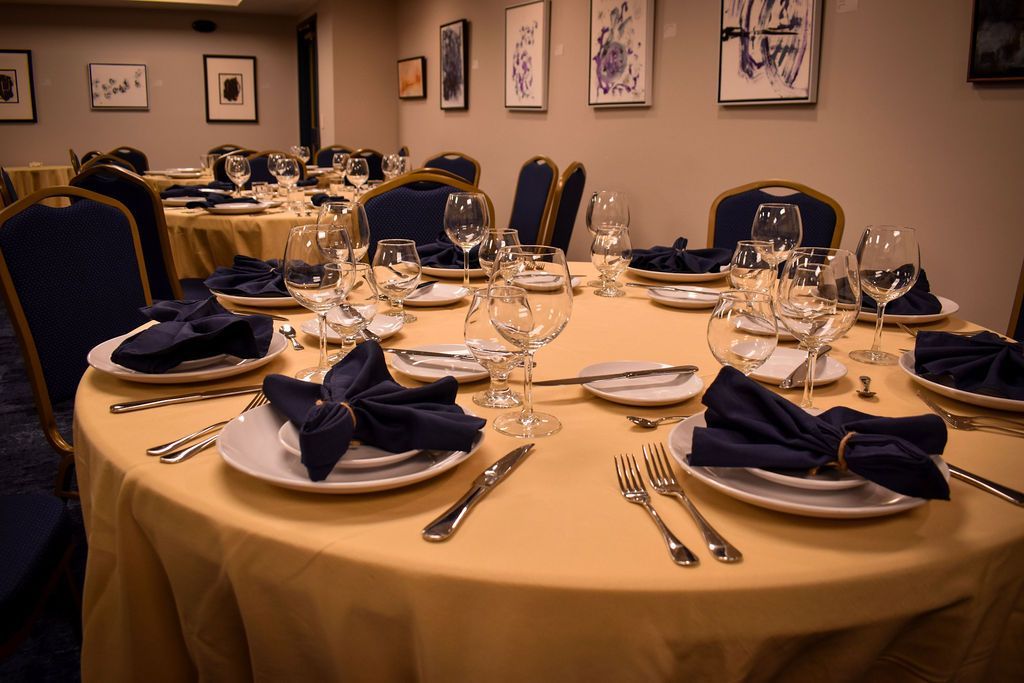 A banquet table set with yellow linens, blue napkins, and glassware in a room decorated with framed art.