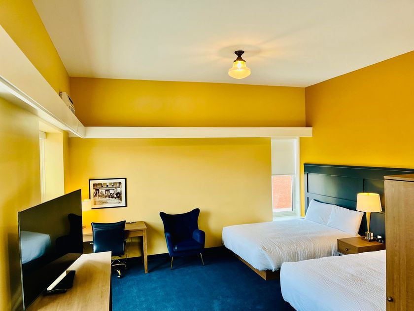 A hotel room with two beds , a desk , a chair and a flat screen tv.