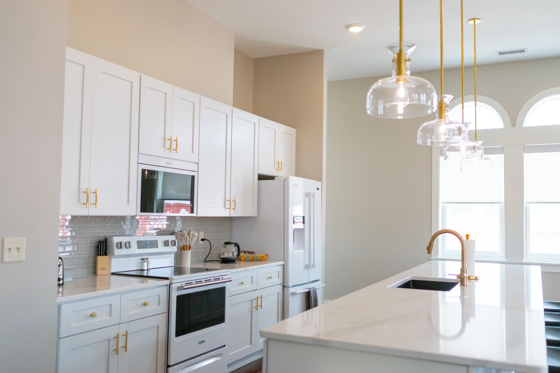 Bright white modern kitchen with island, stainless appliances, pendant lights, and arched windows