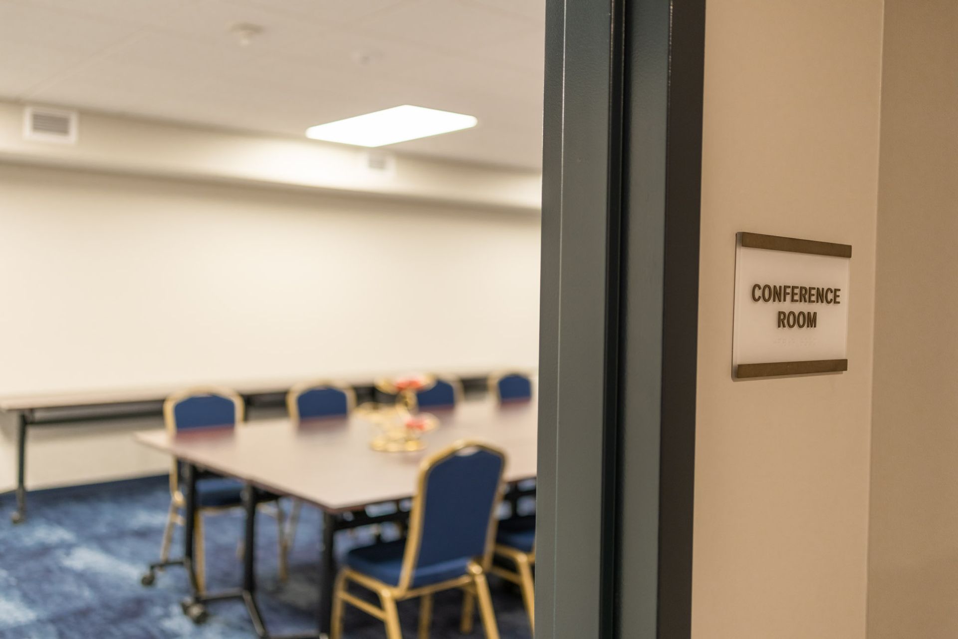 Conference room door with sign. Blurred view of table, blue chairs, and carpet.