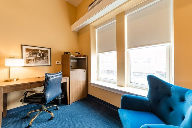 Bright home office with blue chair, wooden desk, lamp, shelving, and large windows
