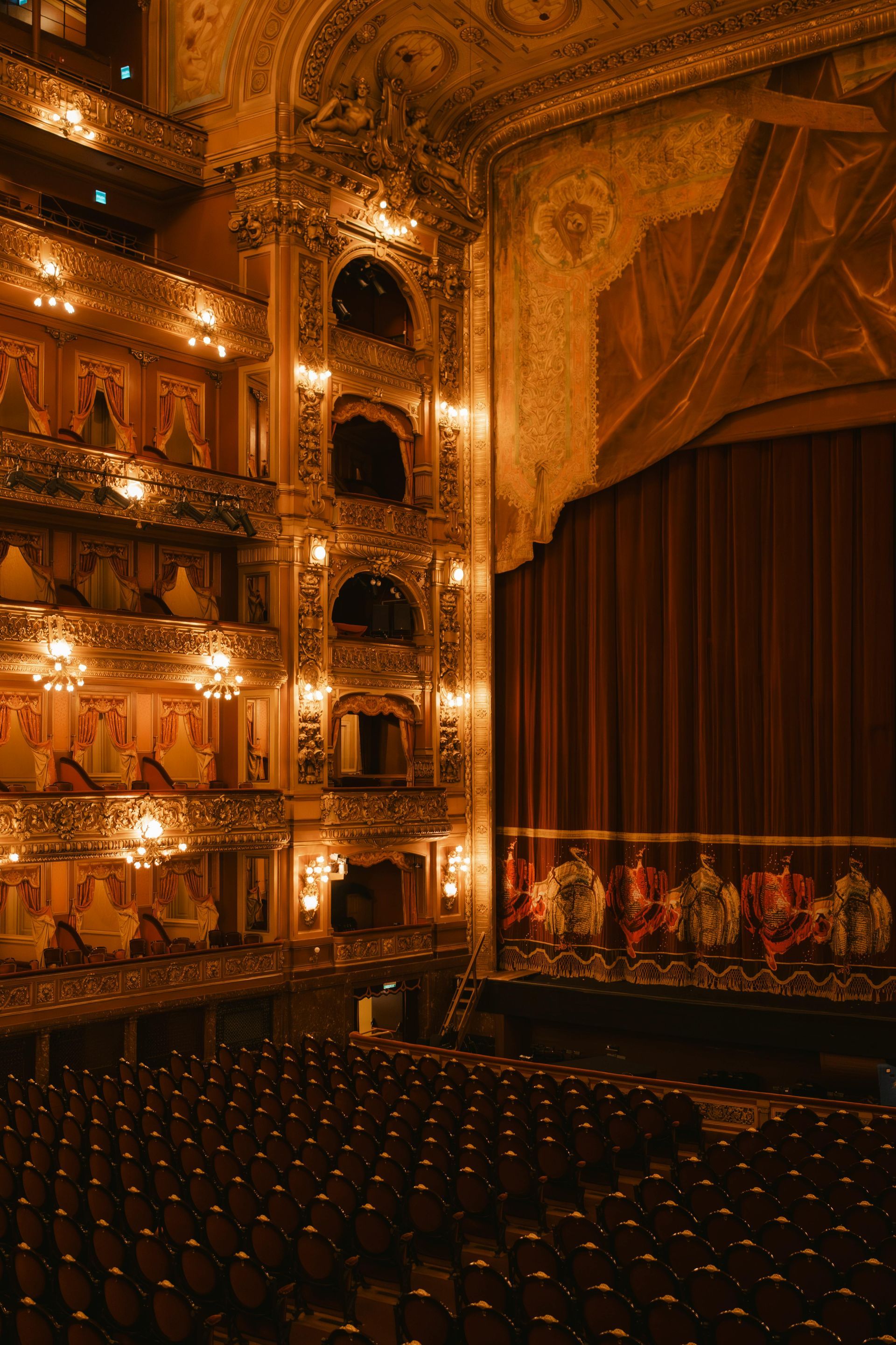 Grand theater interior with ornate balconies, dark red curtains, and rows of seats.
