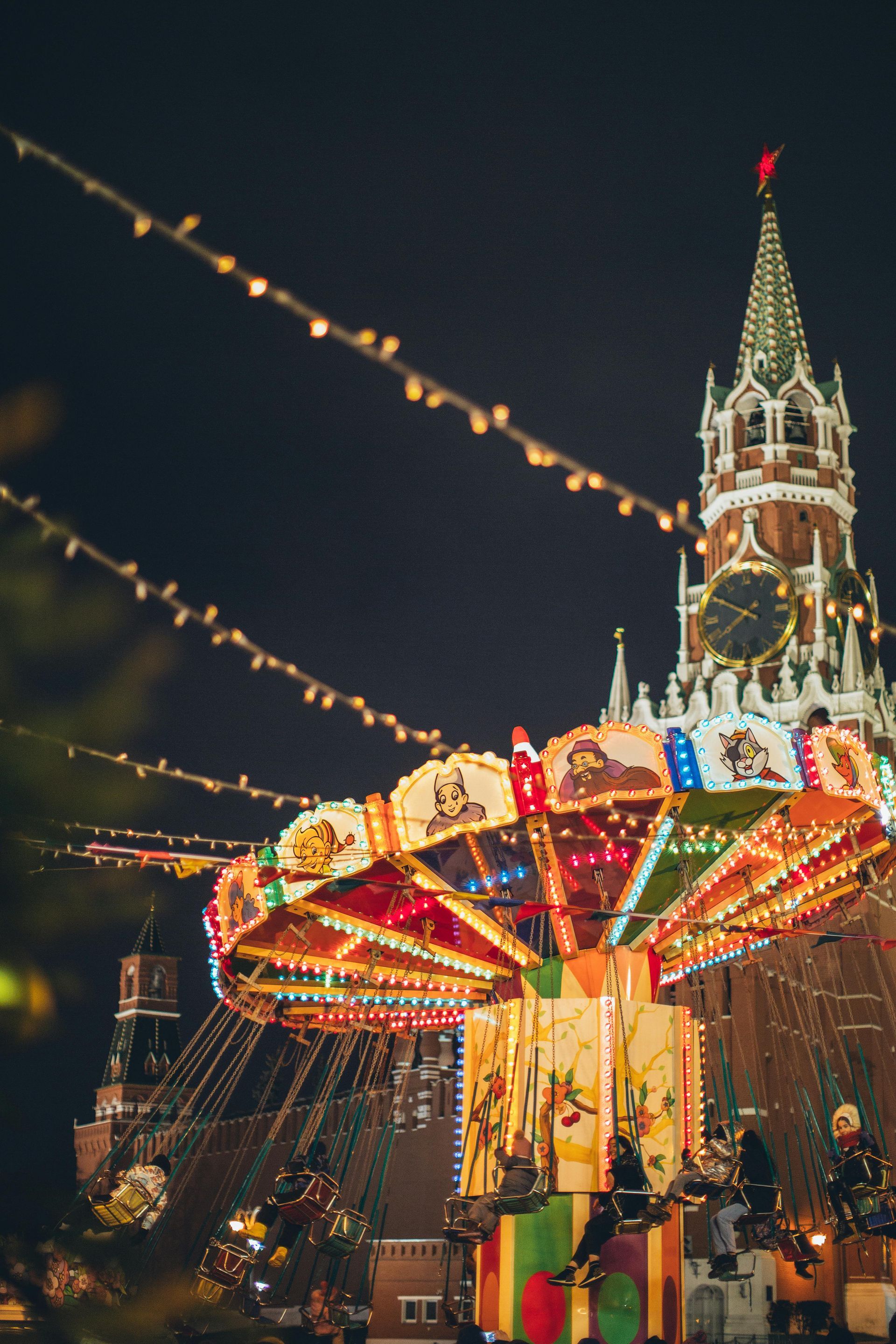 A merry go round is lit up at night in front of a clock tower.