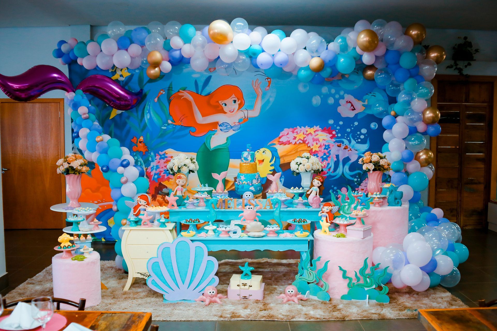 Birthday party with Little Mermaid theme: Ariel backdrop, balloons, desserts.