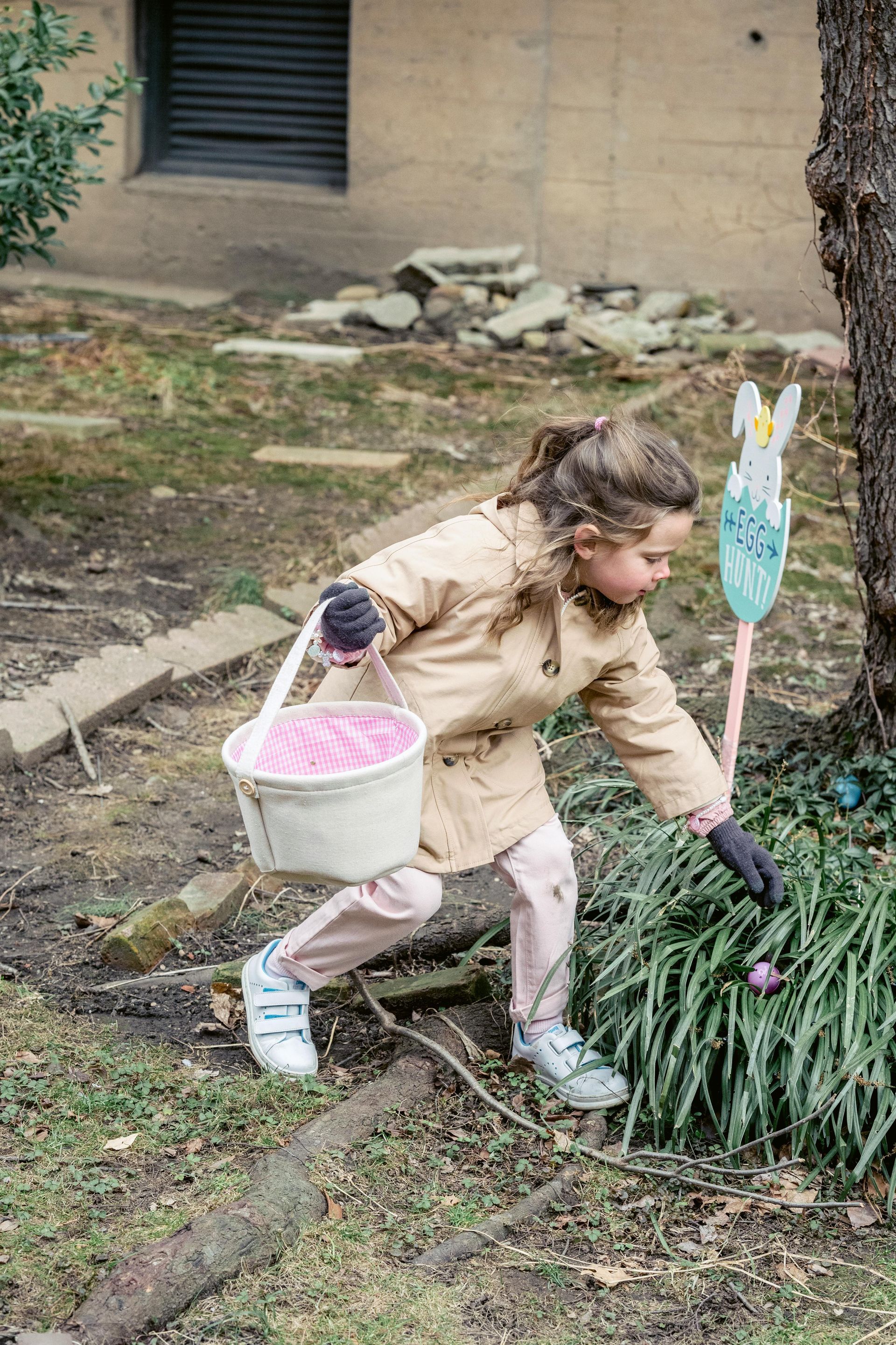 A little girl is picking easter eggs in a garden.