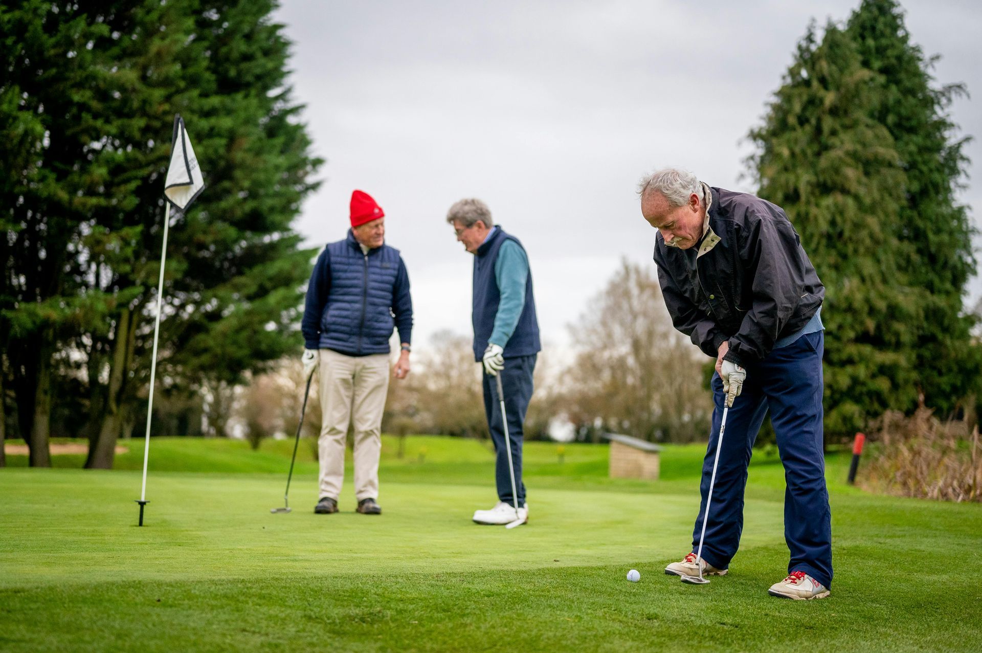Three people on a golf green, one focusing on a putt while the others watch.
