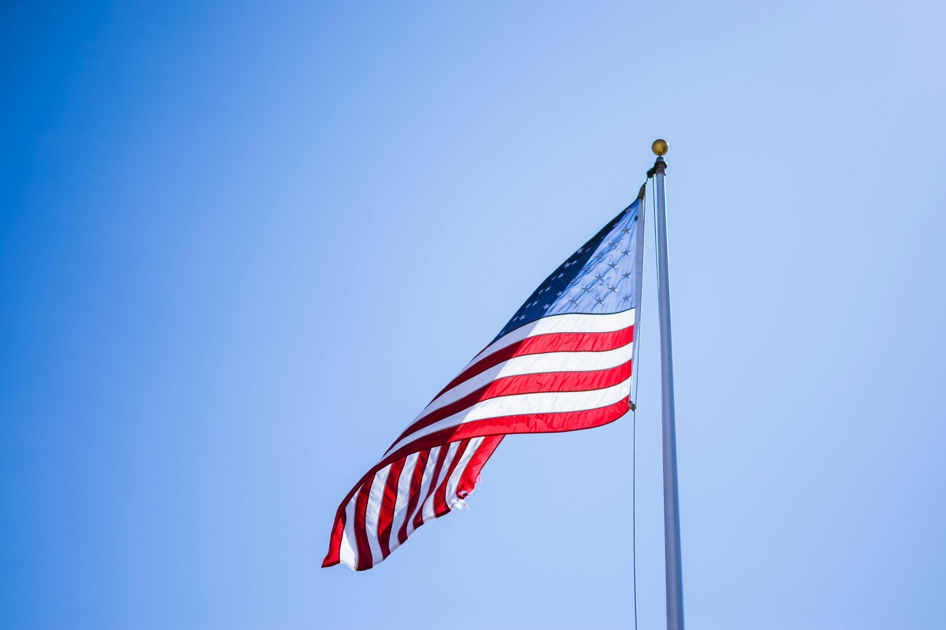 An american flag is waving in the wind against a blue sky.