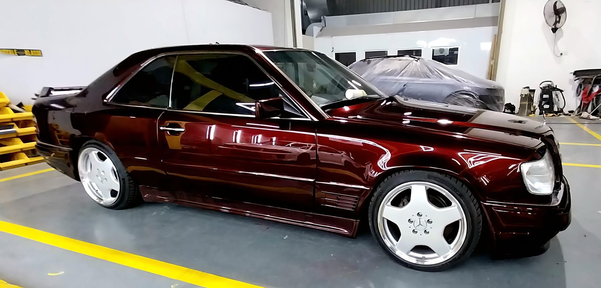 Maroon sports coupe in a garage, with white wheels and yellow floor lines