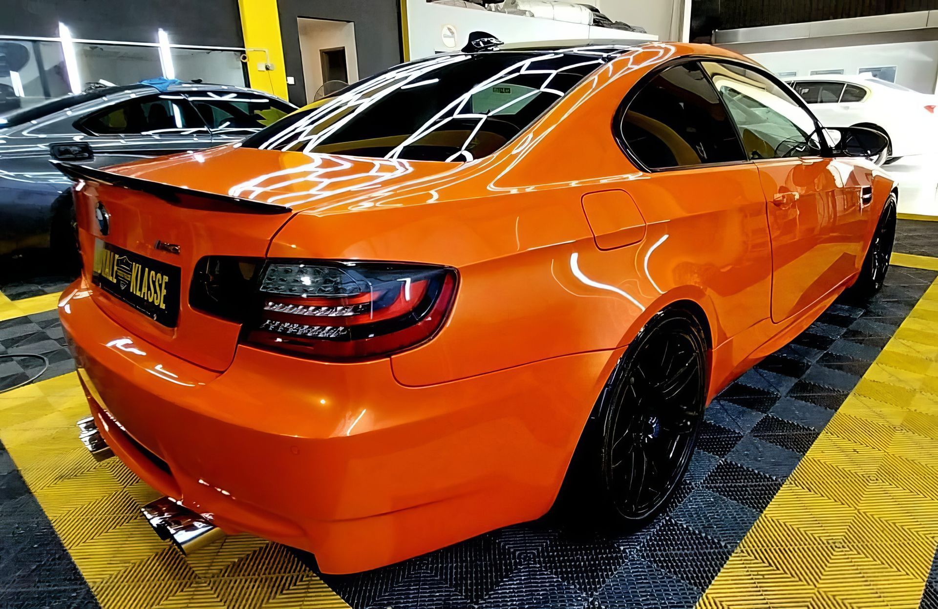 Orange sports sedan in a parking garage, rear three-quarter view with black wheels and tinted windows