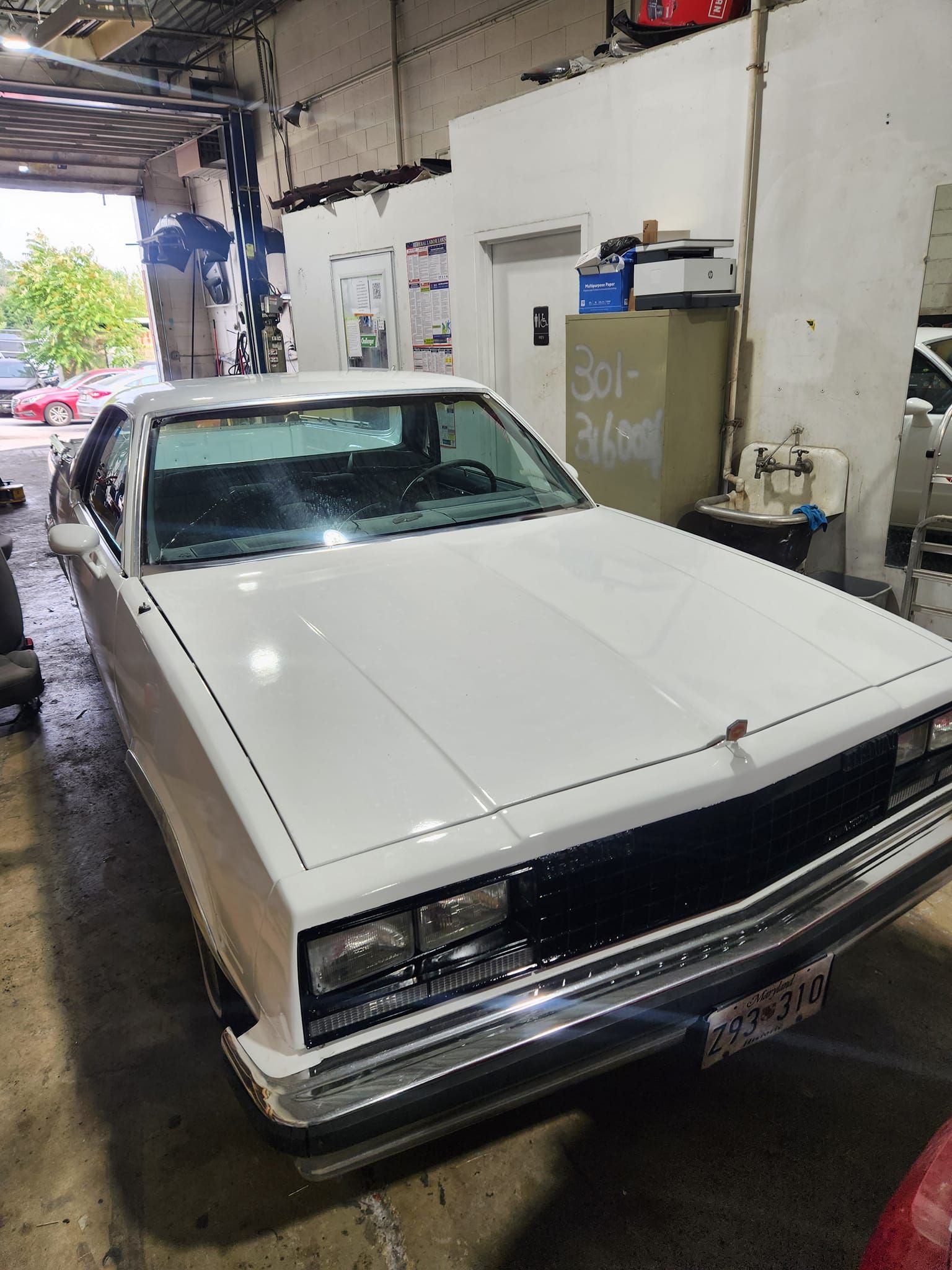 White classic car parked inside an auto garage workshop, viewed from the front-left.