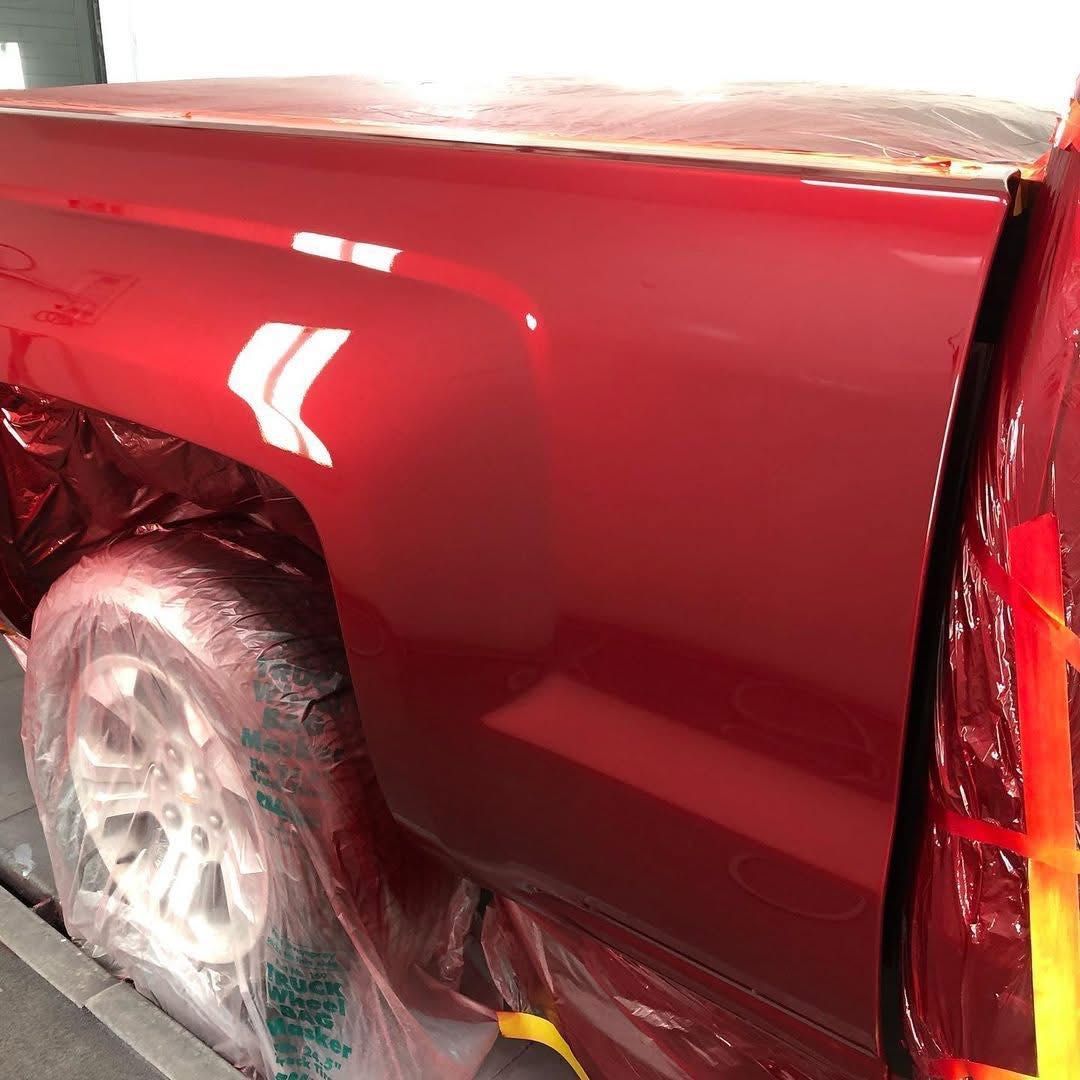 Close-up of a glossy red car body with rear wheel wrapped in plastic in a body shop