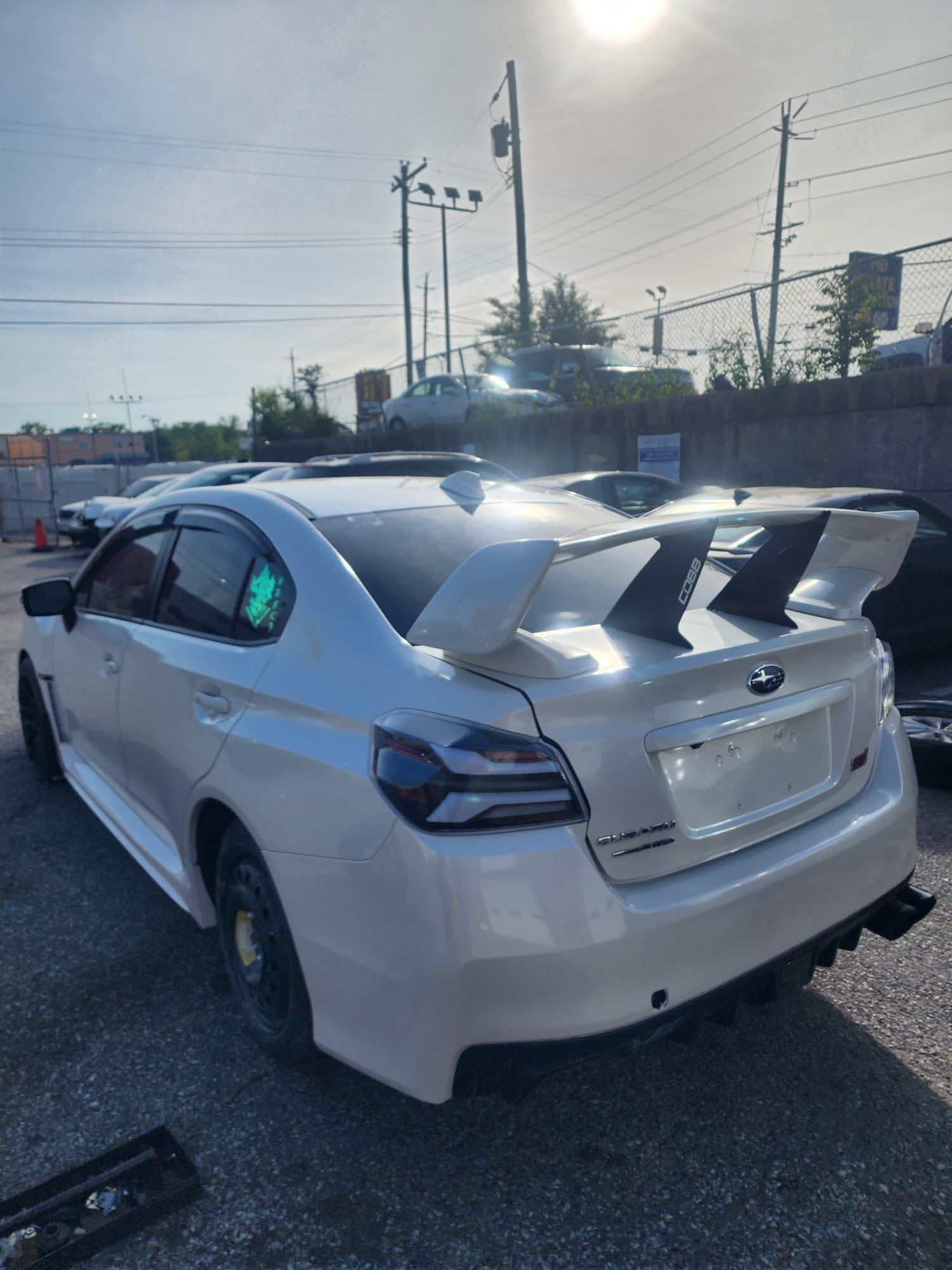 White sedan with a large rear spoiler parked in a lot at sunset.