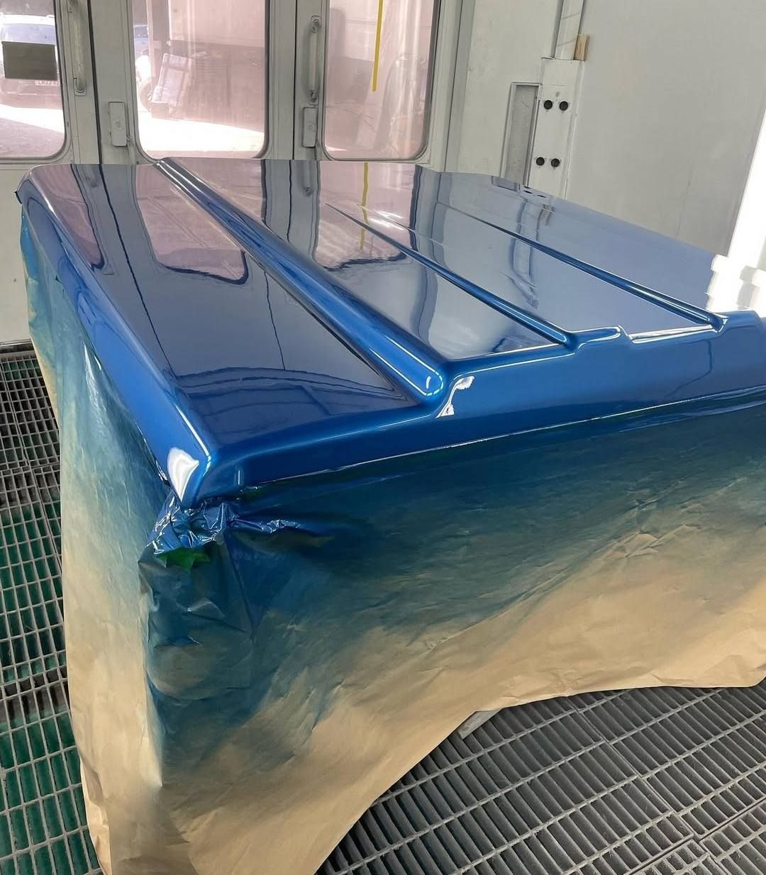 Blue car parts wrapped in plastic drying in a paint booth on a grated floor