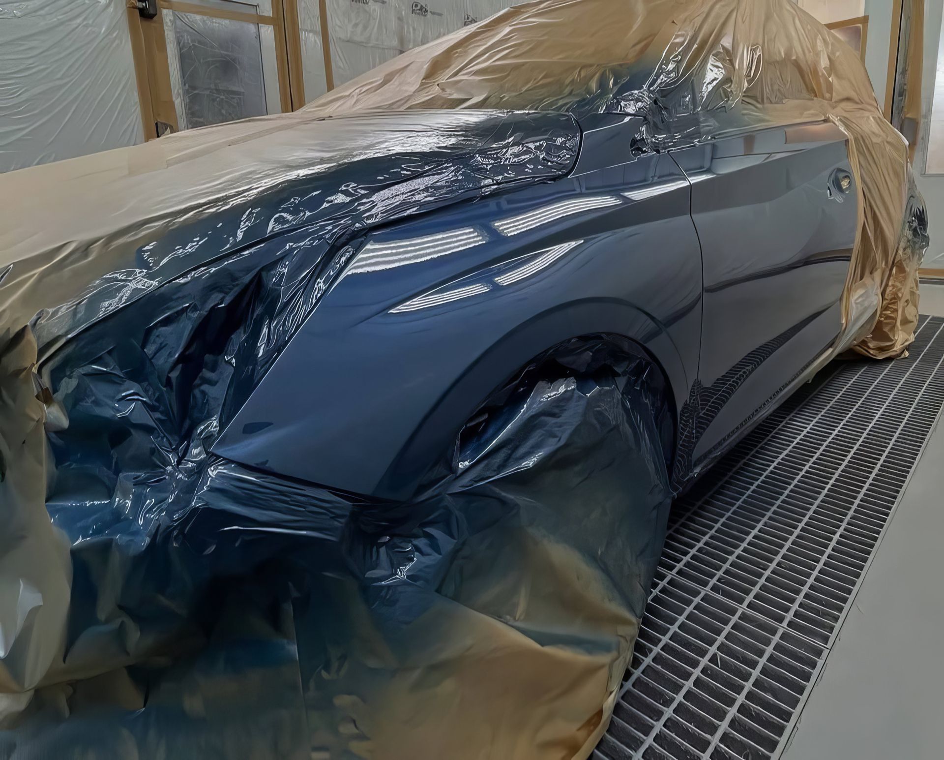 Blue sports car wrapped in protective plastic inside a paint booth