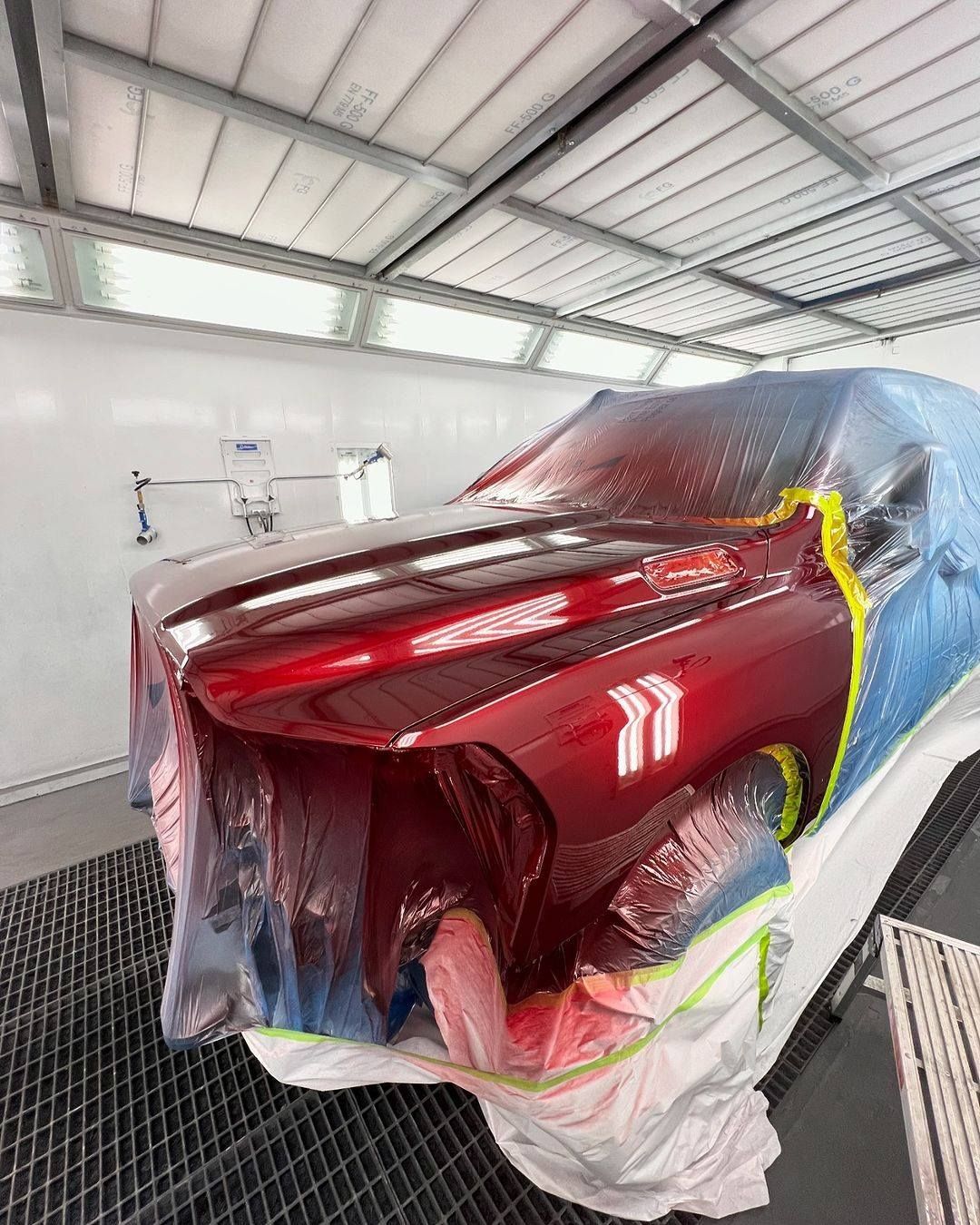 Red car body masked for paint in an auto spray booth, with plastic covering and bright red finish.