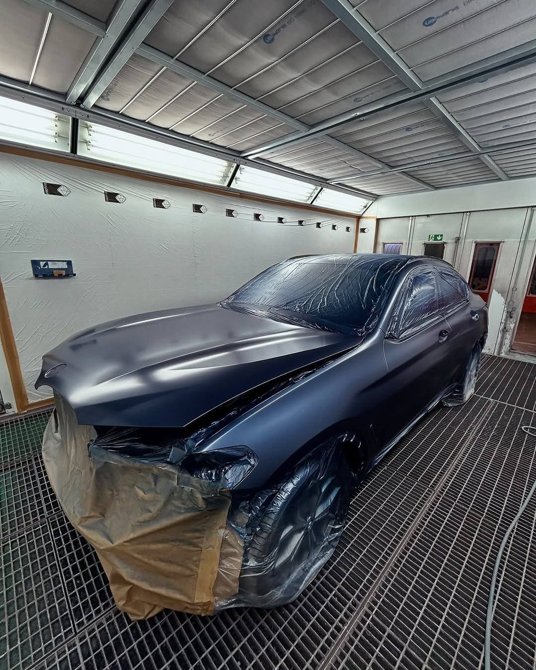 Dark SUV wrapped in plastic inside a garage, with the hood and front covered for painting or repair.