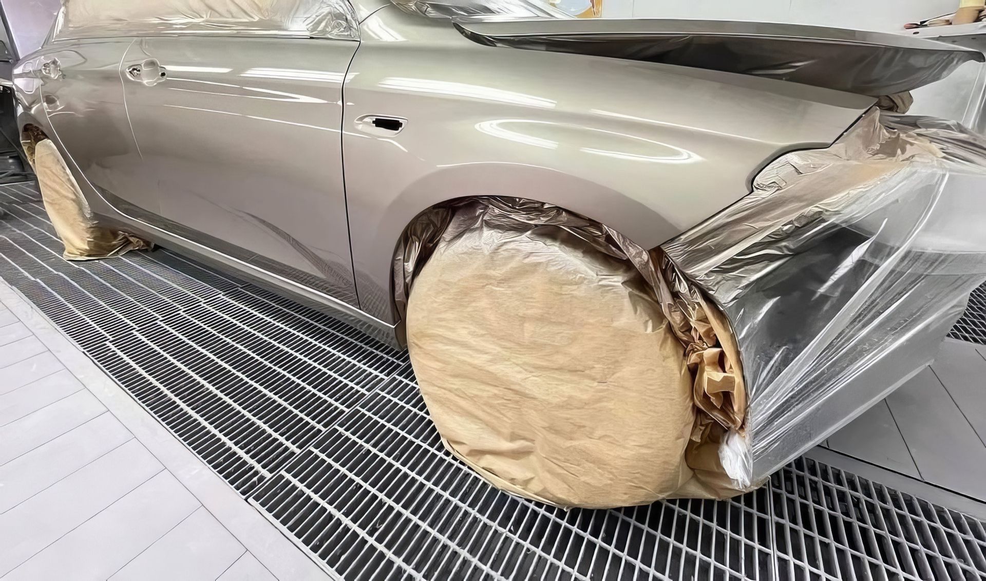 Damaged silver car with front wheel and fender covered in beige repair padding in a workshop