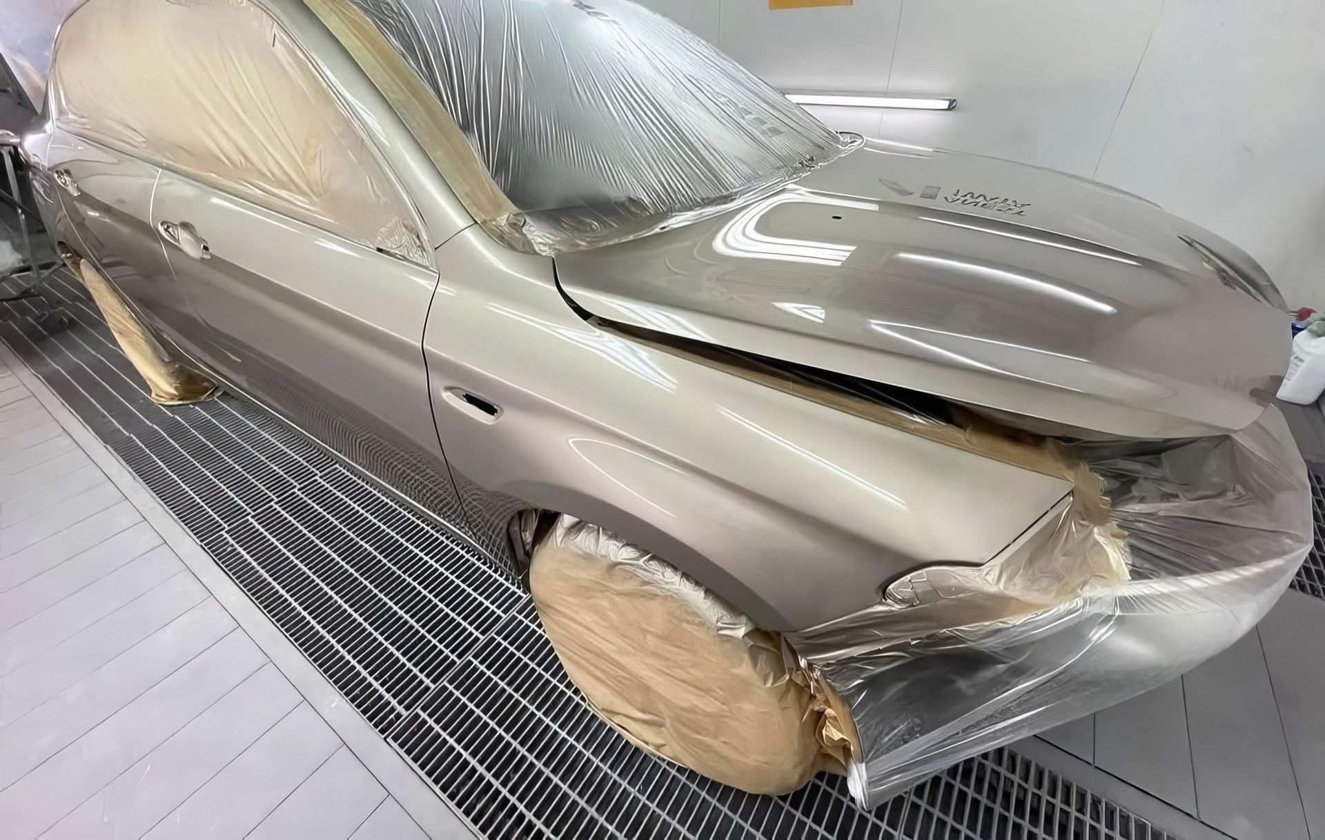 Damaged gray sedan with crumpled front end, hood open, and covered wheels in a workshop bay