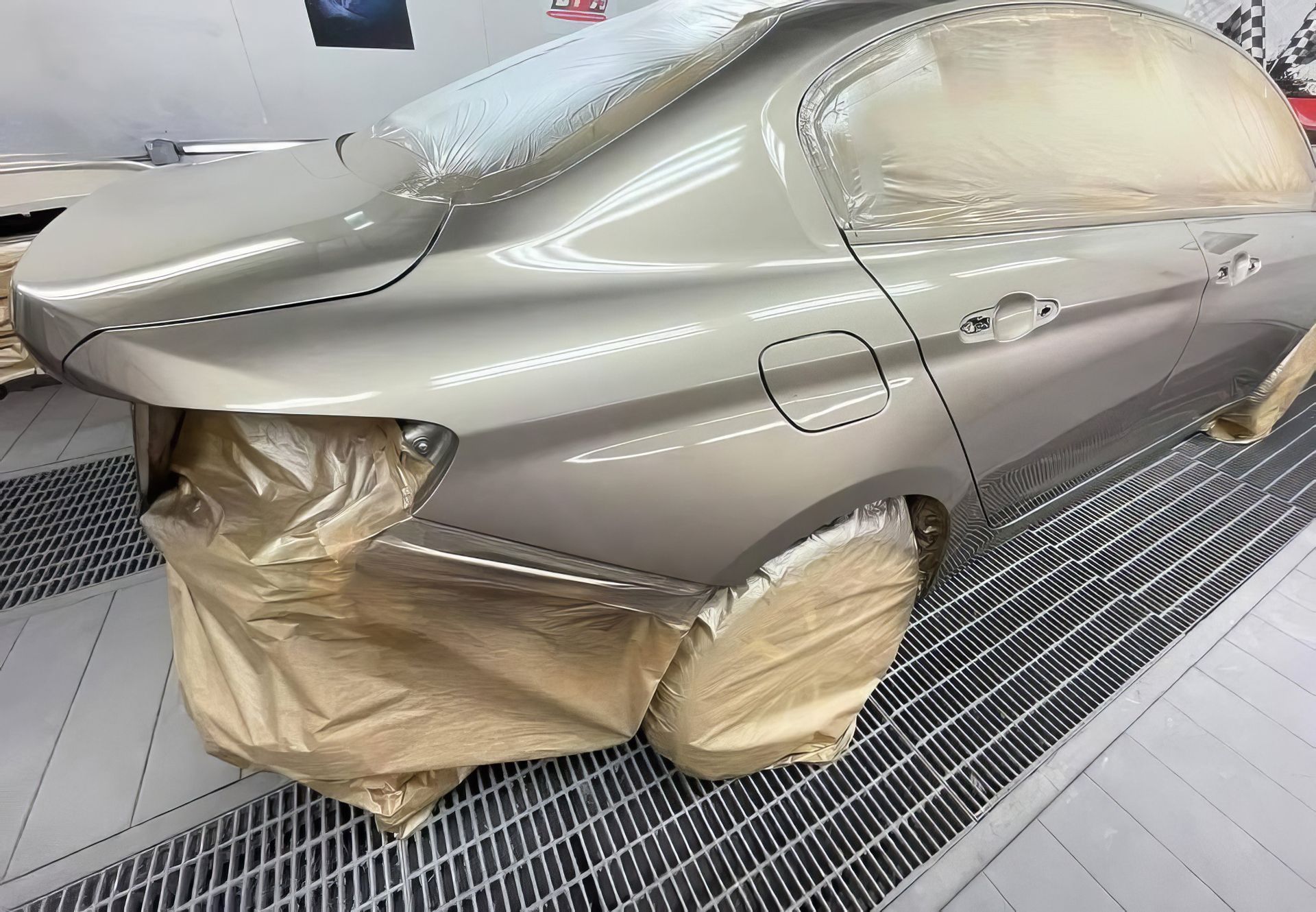 Gray car body masked for paint in a spray booth, with wheels and windows covered in brown paper.