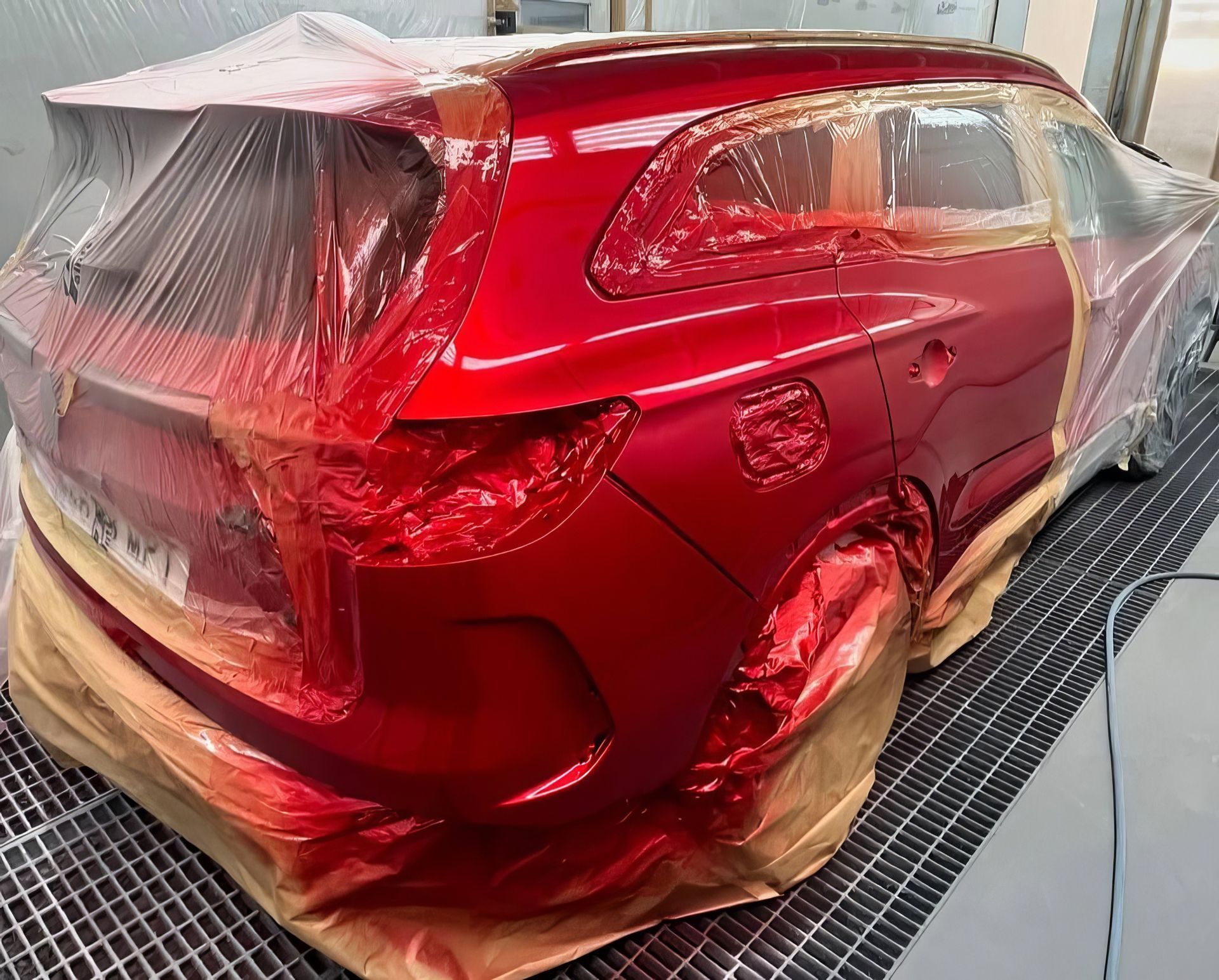 Red car body wrapped in plastic and masked for painting in a workshop booth
