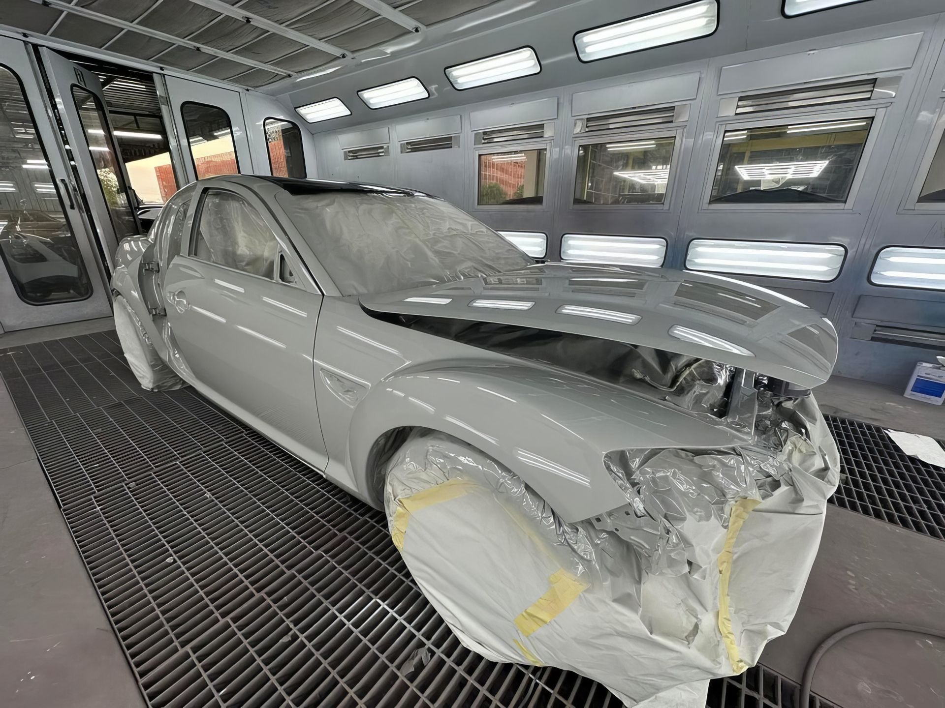 Damaged beige car with crumpled front end and covered wheel in a repair shop