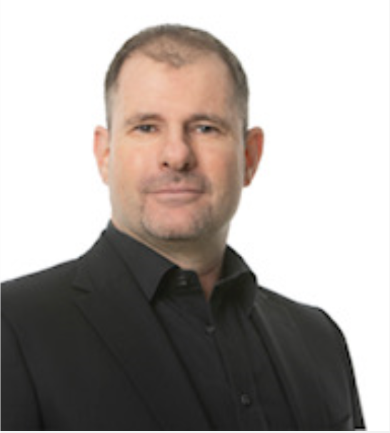 Ein Mann in Anzug und schwarzem Hemd lächelt in die Kamera