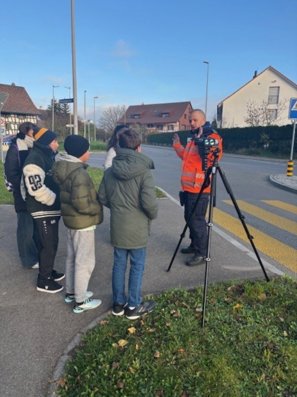 Eine Gruppe von Menschen steht am Straßenrand und unterhält sich mit einem Mann auf einem Stativ