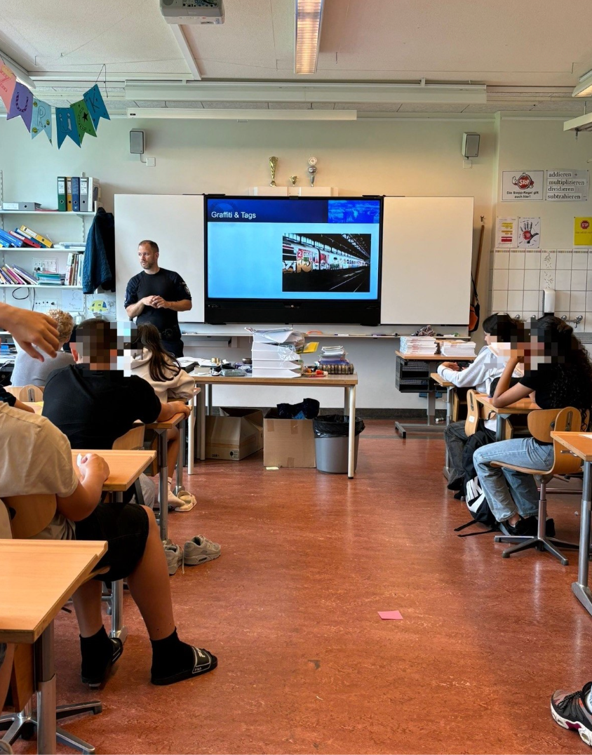 Ein Mann hält in einem Klassenraum vor einer Gruppe von Schülern eine Präsentation.