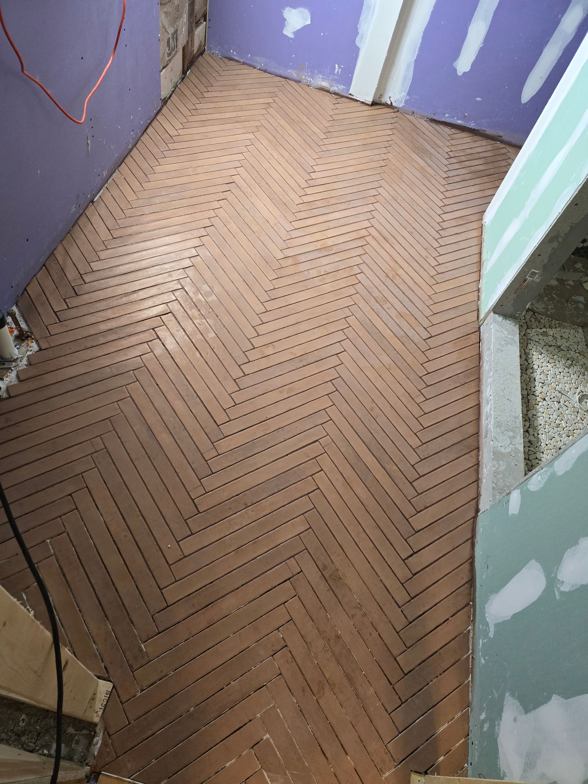 A messy pile of construction debris, scrap wood, metal pipes, and plastic bags on a paved area near a brick wall.