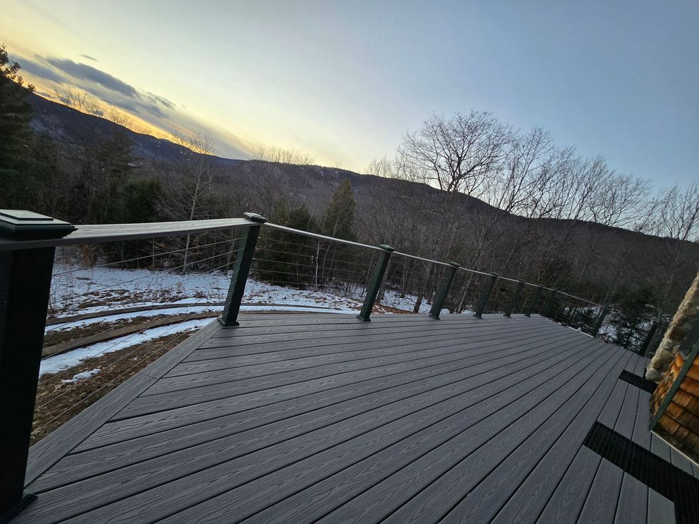 A dark-colored pickup truck towing a black flatbed trailer parked in an empty outdoor lot on an overcast day.
