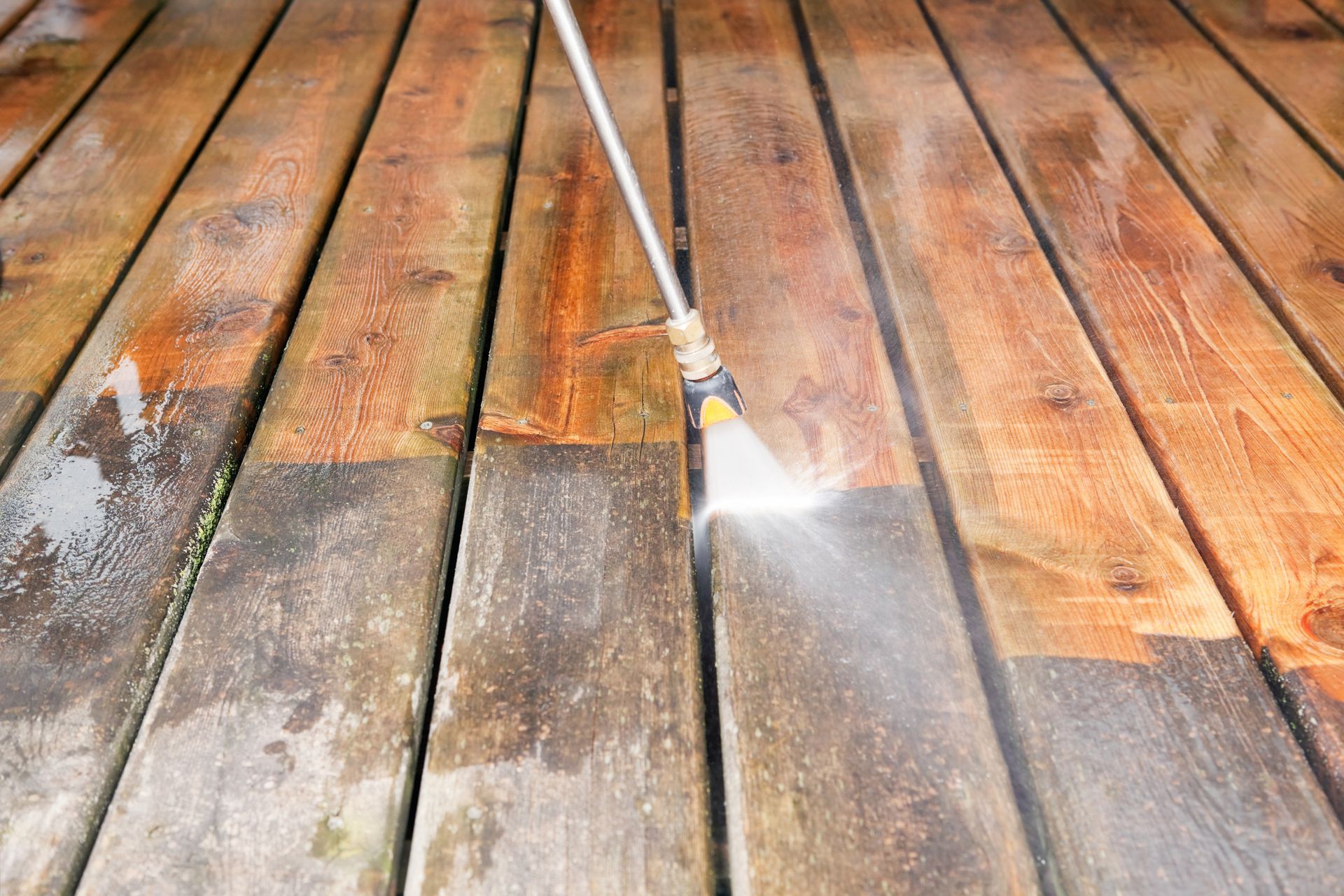 A person is cleaning a wooden deck with a high pressure washer.