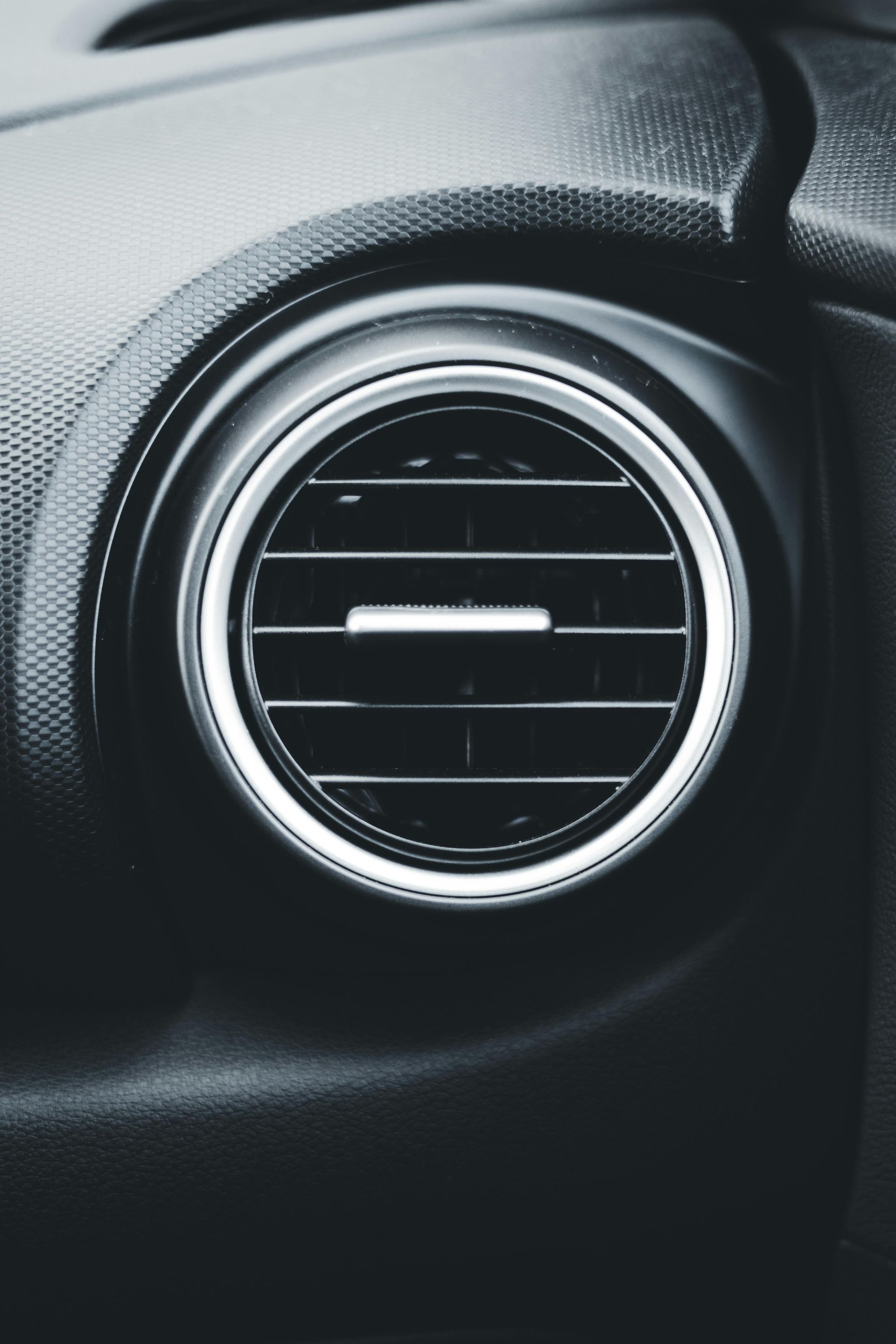 Circular car air vent in a black dashboard with silver trim.