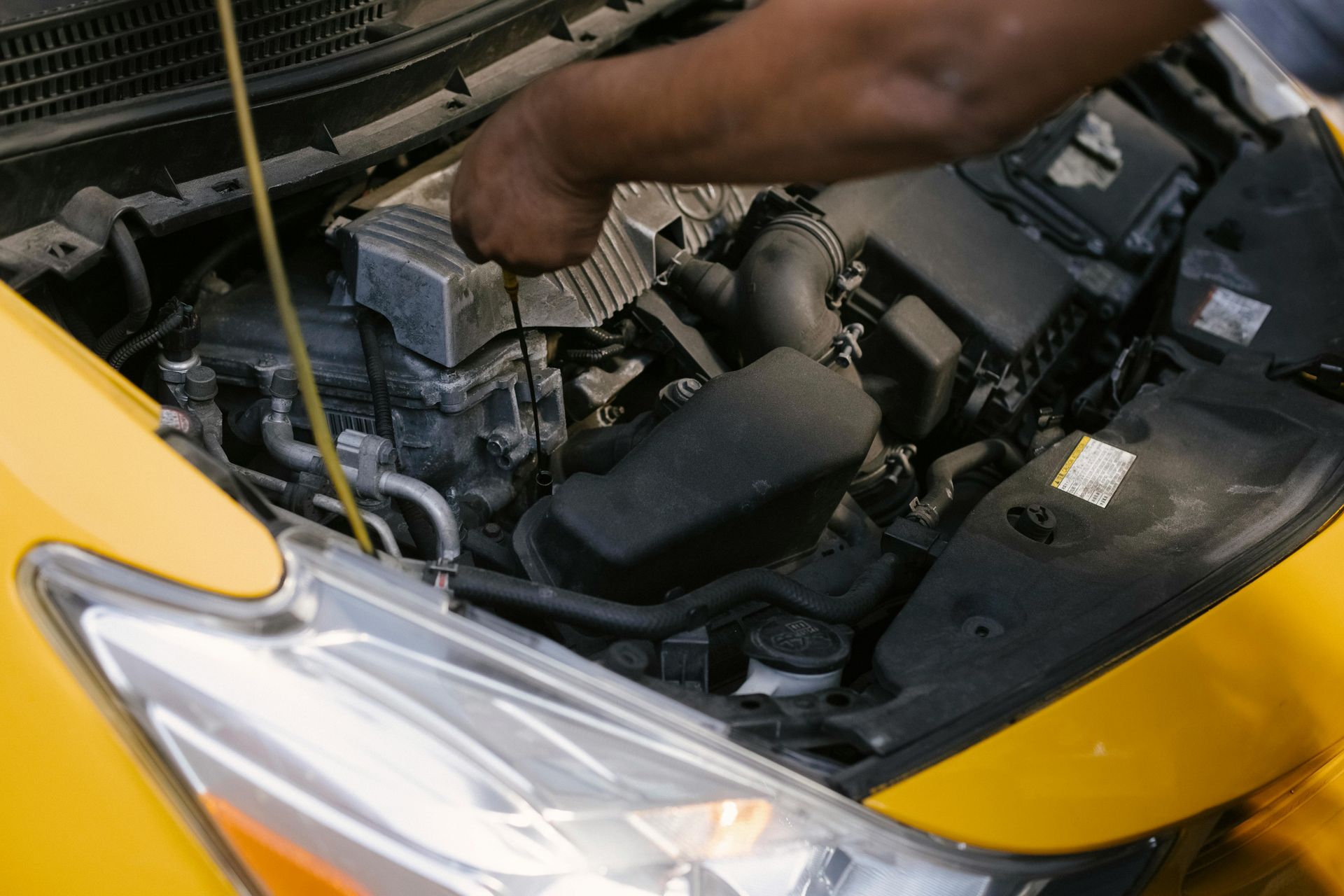 Person checking car engine oil level in a yellow car; hood open.