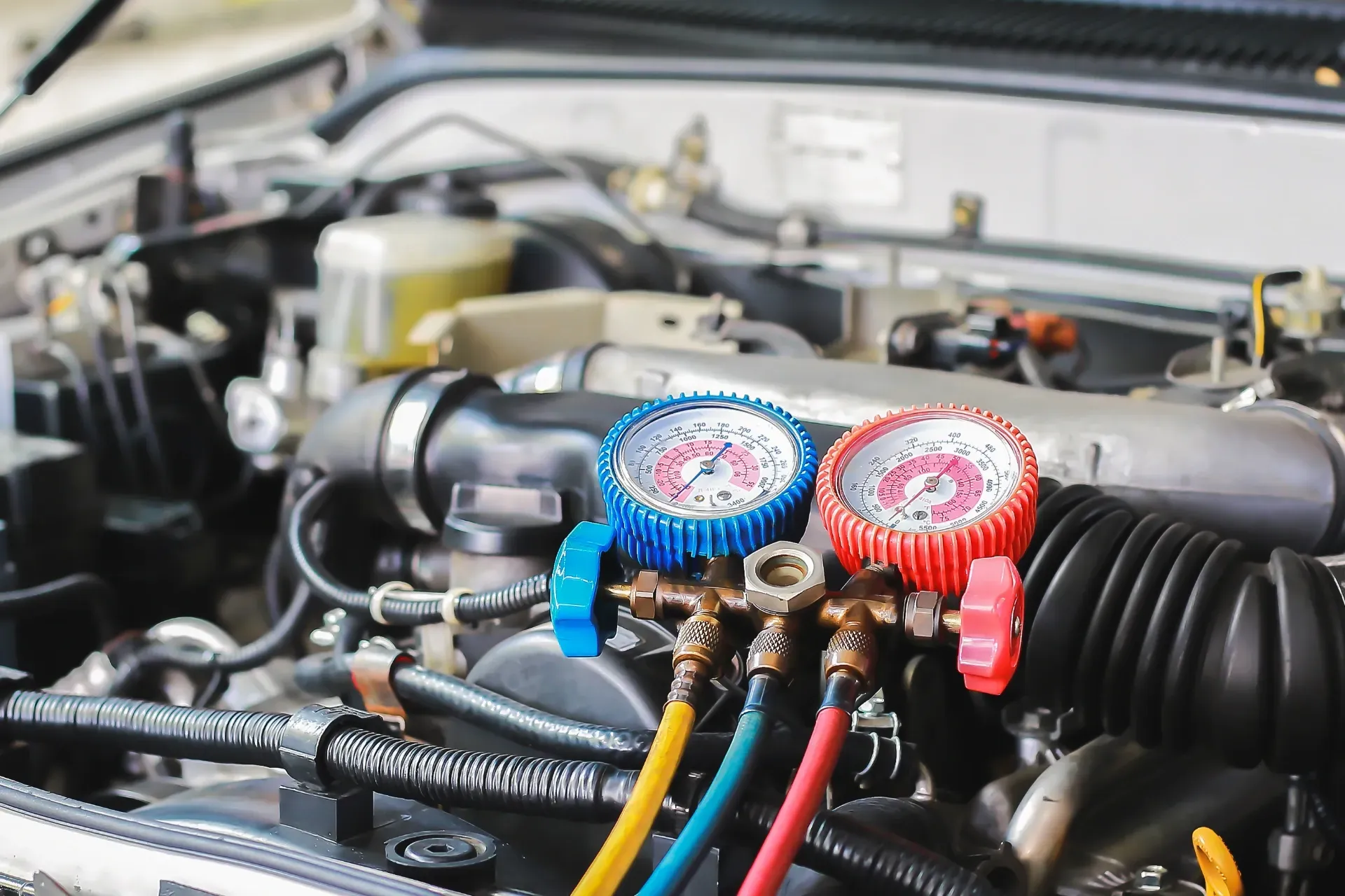 Car engine with gauges attached, measuring the air conditioning system pressure.