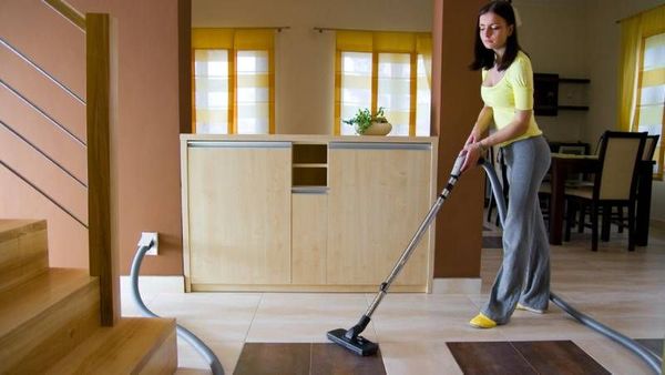 Woman vacuuming a modern kitchen and dining area with hardwood floors and light wood cabinets