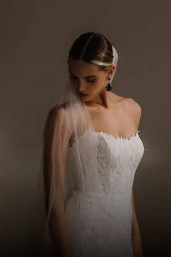 Woman in white lace wedding dress, looking down. She is wearing a veil.