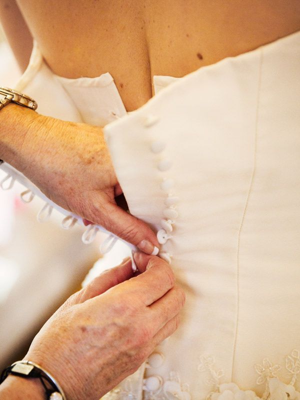 Hands buttoning a white wedding dress.