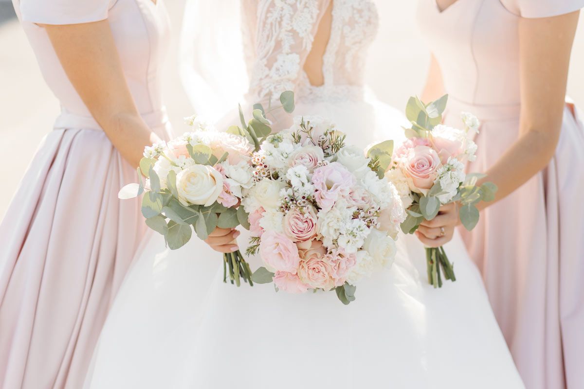 Bride and bridesmaids holding bouquets, wearing light pink gowns.