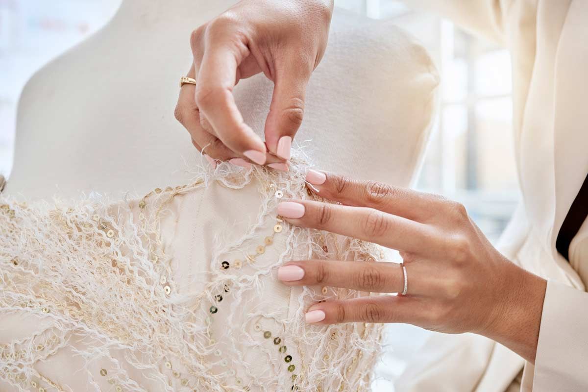 Hands pinning embellishments on a cream-colored dress form.