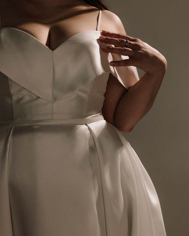 Woman in a white satin wedding dress, hand touching the bodice.