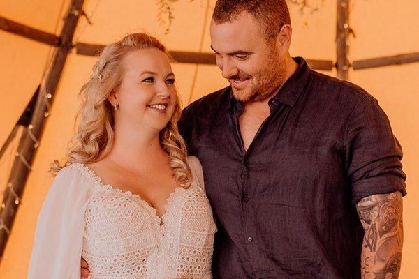 A smiling couple embraces, looking at each other. The woman wears a white dress, the man a dark shirt.