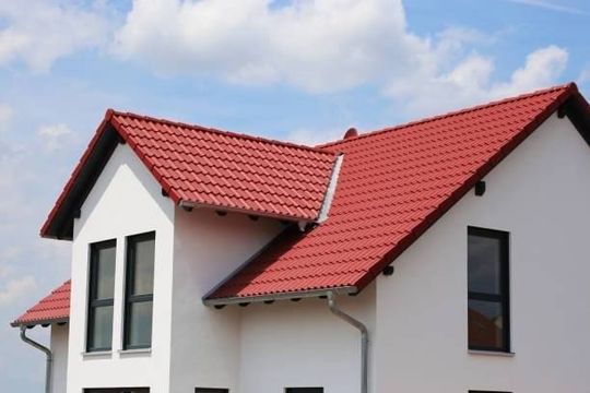 White house with a red tiled roof against a blue sky with clouds.