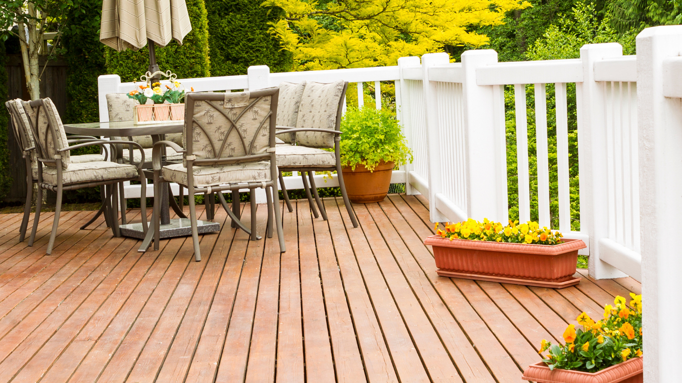 Wooden deck with table, chairs, and potted plants next to a white railing.