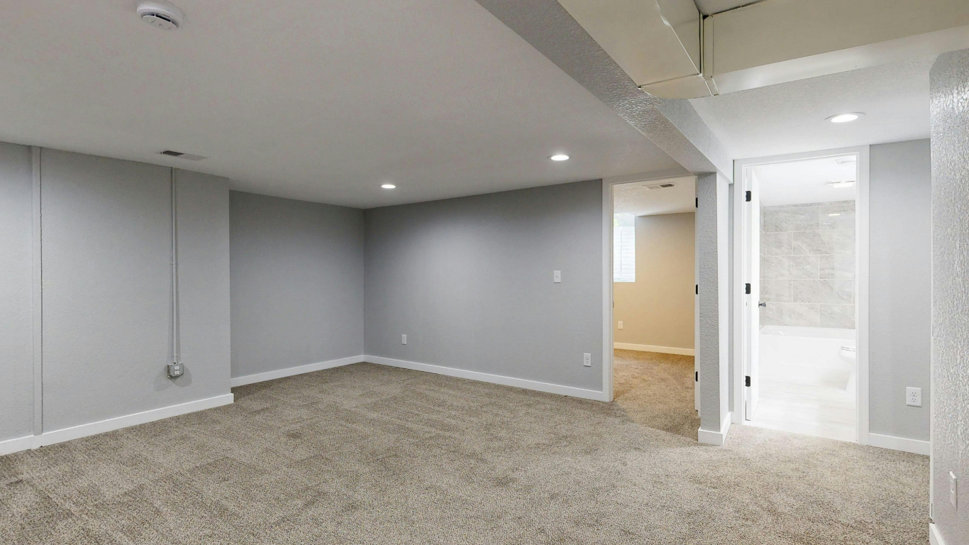 Empty basement room with gray walls, beige carpet, and recessed lighting.