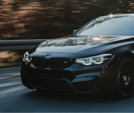 A black car is driving down a road with trees in the background | Ed's Automotive