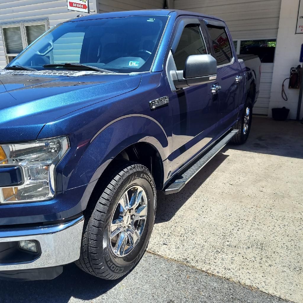A blue ford truck is parked in front of a garage door | Ed's Automotive